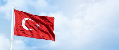 Mavi, bulutlu gökyüzünde Türk bayrağı dalgalanıyor.                               