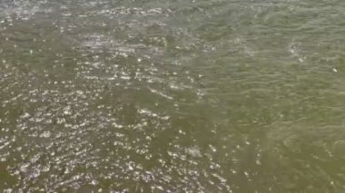 Hafif dalgalı su yüzeyi, su yüzeyinde parlayan güneş tarafından çizildi..