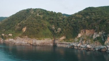 Drone view of the lighthouse in the trees, the white lighthouse building built on the edge of the cliff