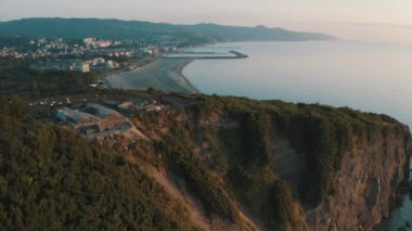 Drone view of the lighthouse in the trees, the white lighthouse building built on the edge of the cliff