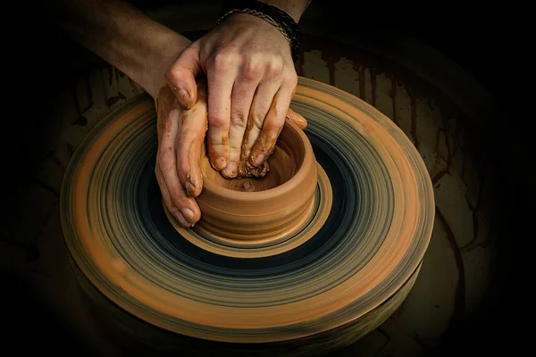 Potter\'s hands while working on the wheel, top view with dark background. Master makes a pot on a potter\'s wheel