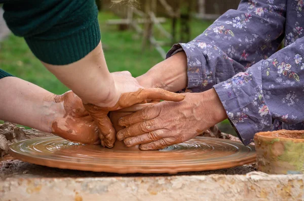 Pottery training. Two pairs of female hands over a potter's wheel in liquid clay. Harmonious contact between master and student