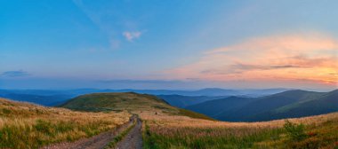 A serene sunset over rolling hills with a winding dirt path leading into the distance. The golden hues of the setting sun contrast beautifully with the cool blue tones of the sky. clipart