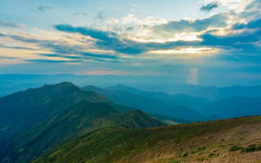Sonbaharın başlarında Karpatlar 'da sakin bir akşam. Güneş ışınları bulutların arasından geçer, dağ sıralarını aydınlatır.