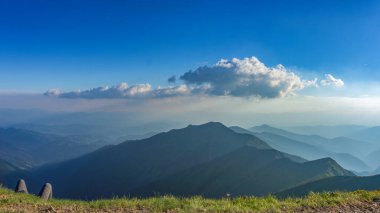 Bir yaz akşamında bir dağ manzarasının manzarası. Dağ yamacında dinlenen bir yürüyüşçünün dizleri patikanın kenarından sarkar.