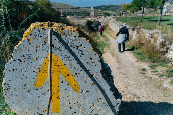 Way Marking Stone Post with Scallop Shell Symbol and Yellow Arrow Sign in the Spring Field outside Sarria, Galicia on the Trail of the Way of St James Pilgrimage Trail Camino de Santiago.