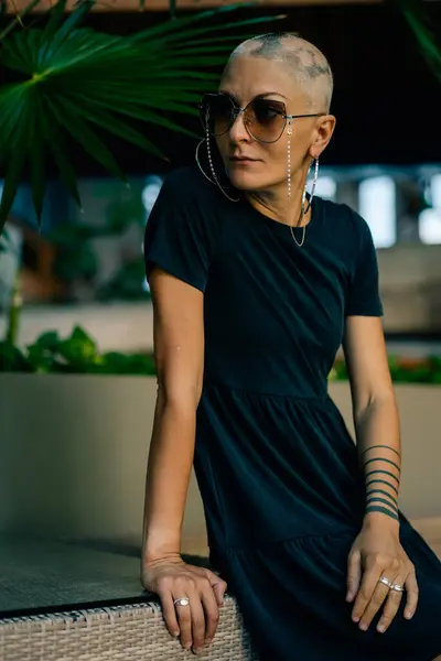 stock image A serious young girl with no hair in a black dress and sunglasses, looks away. High quality photo