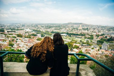 Kızlar sırt çantasıyla oturur ve Tiflis, Georgia şehrini seyrederler. Yüksek kalite fotoğraf