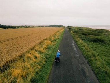 Aerial shot of a female cyclist crossing fields in England. High quality photo clipart