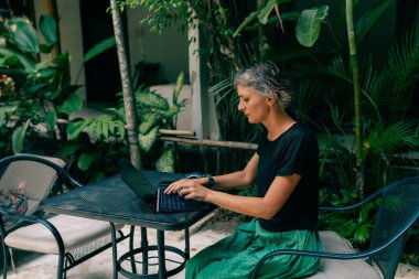 Tropik bir ülkede uzaktan çalışma. Laptopla çalışan kadın kafeteryada orman manzaralı, hindistan cevizi palmiyeli oturuyor. Yüksek kalite fotoğraf