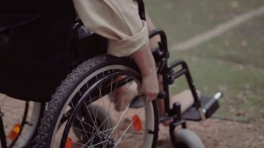 Tekerlekli sandalyedeki engelli bir kız kolu hareket ettiriyor. Gün boyunca parkta.
