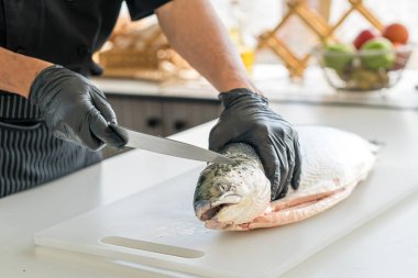 The chef cuts the salmon on the table. Male cooks preparing sasimi in the restaurant kitchen.