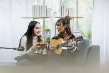 Oturma odasında gitar çalan iki genç kadın..