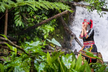 Hmong Hill kabilesi kıyafetleri. Genç bir tepelik kabile kadını şelalede suyun üzerinde oturuyor..