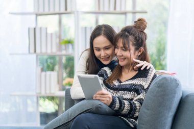 Genç kadın çiftler tablet üzerinde başvuru kullanıyor. Kanepede dinlenen bir kadın..