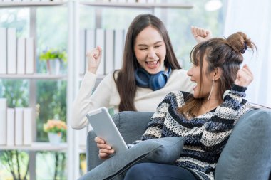 Sevinen birkaç kadın. Konuşan ve sevinen iki genç kadın. İki kadın oturma odasındaki kanepede tablet kullanıyor..