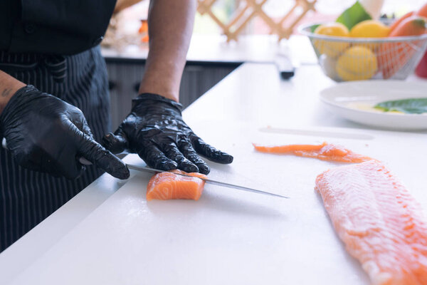 Japanese Chef preparing a fresh salmon fillet in kitchen. A worker cutting salmon on a board.