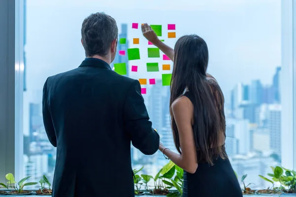 Business people working and use post it notes to share idea on the glass window in office. Businessman and Businesswoman work on project planning board.