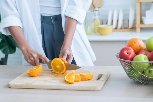 Cooking vegan food. Chef is cutting orange to decorate a salad. A woman is cutting an orange on a wooden cutting board.