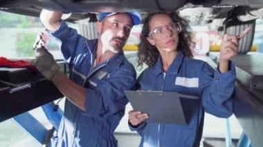 Servis arabası makine konsepti. İki üniformalı tamirci kaldırılmış araçla otomobil servisinde çalışıyor..