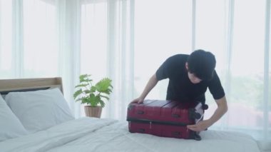 Genç adam seyahat etmek için memnuniyetle bavulunu topluyor. Tatil için bavul hazırlayan bir adam..