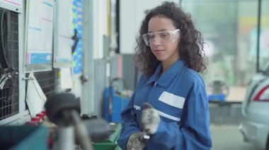 Kadın bir oto tamircisi arabanın önünde duruyor ve elinde bir tornavida tutuyor..