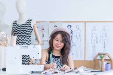 Genç moda tasarımcısı stüdyosunda yeni bir elbise üzerinde çalışıyor. Dikiş makinesinin başında oturan şık bir atölyenin genç Asyalı çalışanı.