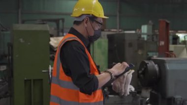 Fabrika işçisi. Torna fabrikası. Mühendis erkek işçi fabrikada çalışıyor. Envanter verilerini cep telefonuyla kontrol ediyor..