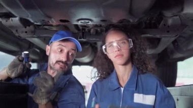 Otomobil servisi. Üniformalı tamirciler otomobil servisinde çalışırken arabayı inceliyorlar. Müşteri arabalarının motoru garaja getirildi..