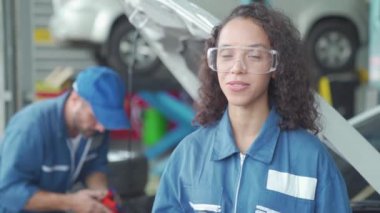 Kadın bir tamirci araba tamir hizmetlerinden bahsediyor. Tamirci atölyedeki arabanın yağını değiştiriyor..