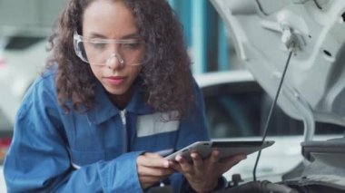 Tamirci motor yağını kontrol ediyor. Kadın oto tamircisi hataları tanımlamak için özel bir tablet bilgisayar kullanır.