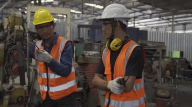 Young man and Young woman are discussing in industrial plants. Engineer with clipboard and tablet on hand to see how the machine works.