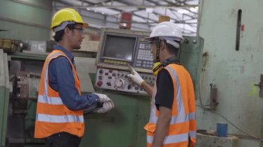 Fabrika işçisi. Genç mühendis, ağır makineyi fabrikada otomatik torna tezgahına doğru çalıştırıyor..