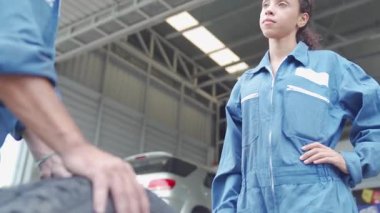 Oto tamirhanesinde araba tamircisi asistanı olan erkek ve kadın tamirci. İki el birbirine dokunuyor..