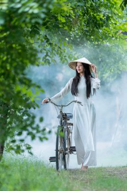 Kırsalda bisikleti olan ulusal kostümlü Vietnamlı bir kız. Ao dai, Vietnam 'da kadınlar için ünlü bir geleneksel kostümdür..