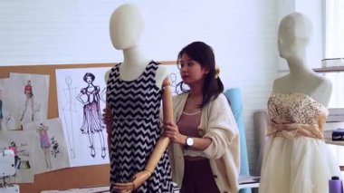 Tasarımcı stüdyoda kıyafet üretir. Genç bir kadın tasarlanmış bir elbiseyi bir mankenin üzerinde deniyor..