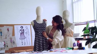Tasarımcı stüdyoda kıyafet üretir. Genç bir kadın tasarlanmış bir elbiseyi bir mankenin üzerinde deniyor..