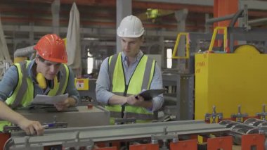 Kasklı ve kasklı bir işçi. İş prosedürü kontrol listesi için pano ile çalışan imalat işçisi.