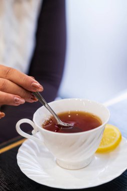 Bir kadının eli paslanmaz çelik bir kaşık tutuyor ve sıcak çay karıştırıyor.