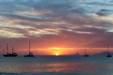 Formentera, Balearic Adaları 'ndaki Ses Illetes plajına yakın harika bir gün batımı (görünür marka veya logo yok, sadece yelkenli teknelerinde ulusal bayraklar).