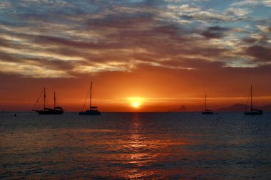 Formentera, Balearic Adaları 'ndaki Ses Illetes plajına yakın harika bir gün batımı (görünür marka veya logo yok, sadece yelkenli teknelerinde ulusal bayraklar).