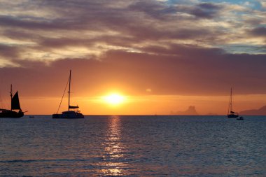 Formentera, Balearic Adaları 'ndaki Ses Illetes plajına yakın harika bir gün batımı (görünür marka veya logo yok, sadece yelkenli teknelerinde ulusal bayraklar).