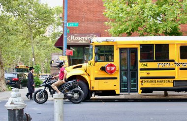 Williamsburg, Brooklyn, NYC, ABD - 18 Ağustos 2022: Aşırı ortodoks bir yayanın, yaygın bir motorsikletçinin ve Lee Bulvarı 'nda yeşil ışık bekleyen tipik bir okul otobüsünün karşıt görüntüsü.