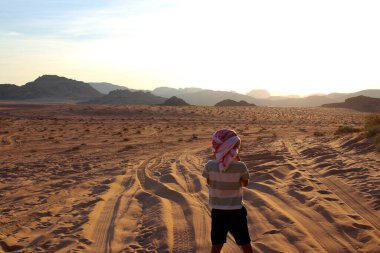 Küçük bir çocuk Wadi Rum çölünde muhteşem bir gün batımının tadını çıkarıyor. Ürdün 'ün en harika yerlerinden biri..