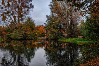 Güzel eski tuğla su değirmeni ve gölet. Sarı ve kırmızı yapraklı sonbahar kırsalları