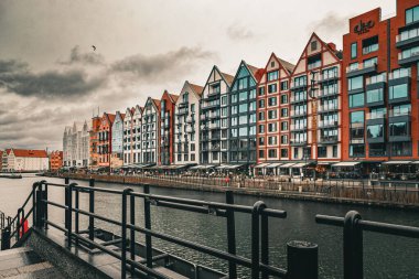Gdansk, Polonya - 17 Kasım 2024: Gdansk 'ın tarihi simgesi, ortaçağ tuğlalı gotik evleri ve Motlawa nehrinin seti üzerinde modern apartman inşaatı. Dramatik yağmurlu sonbahar gökyüzü