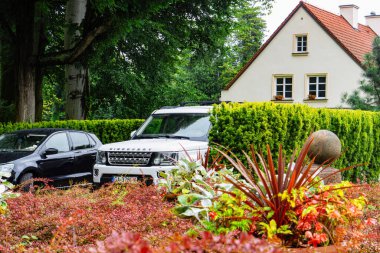 Gdansk, Polonya - 30 Ağustos 2025: Avrupa 'nın varlıklı banliyösü. Konut kulübesi ve park etmiş bir Land Rover arabası yeşil lanet parkın arasında.