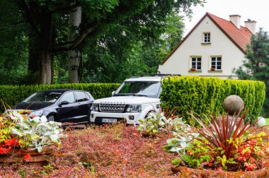 Gdansk, Polonya - 30 Ağustos 2025: Avrupa 'nın varlıklı banliyösü. Konut kulübesi ve park etmiş bir Land Rover arabası yeşil lanet parkın arasında.