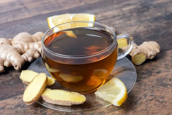 Dilimlenmiş limon ve şeffaf çay fincanında zencefil kökü ile çevrili, ahşap masada zencefil tişörtü., 