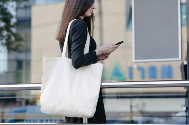 Kentsel şehir arka plan karşı beyaz tekstil eko çanta tutan kadın. Ekoloji veya çevre koruma kavramı. Sahte için beyaz eko çanta.